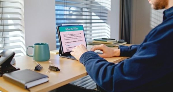Man sitting at a desk typing on a tablet displaying a page of the digital journal titled The Comparison Reset. A green mug, books, and office supplies sit nearby, highlighting a calm workspace for completing an interactive journal.