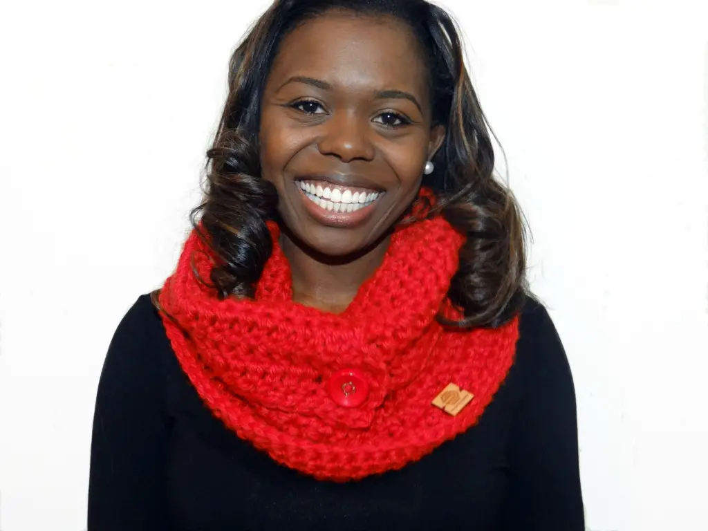 A woman smiling and wear a red chunky crochet cowl with a large round button.