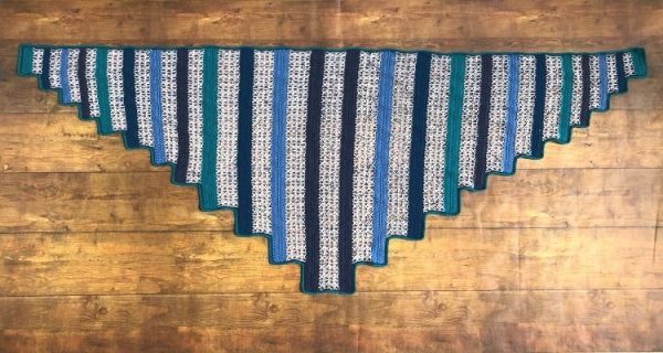 A flat lay of a triangular shawl made with alternating sections of solid color and lacy stitches.