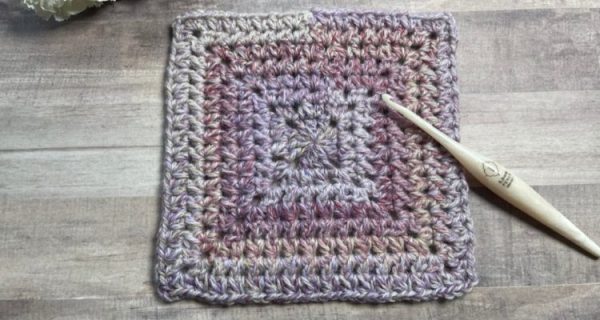 Juneberry Crochet Square is worked from the center out with a yarn that transitions from grayish-purple to purple and back to the grayish-purple color.