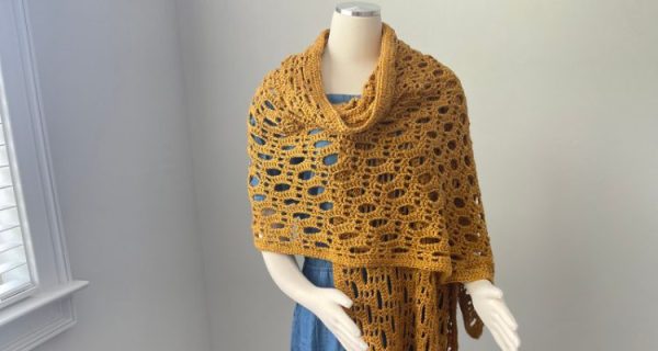 A lacy gold crochet wrap is displayed on a mannequin.