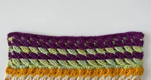 A close up picture of a 3-d crochet stitches in a mint green and purple. The stitches look similar to a raspberry and lean to the left on one row and then lean right on the next row in this crochet scarf.