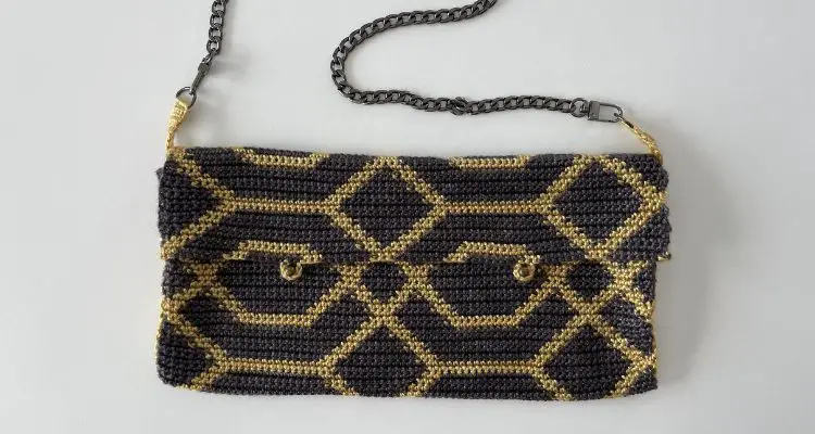 The Shuri Crochet Purse Pattern is intriguing with a geometric pattern all over created with black and gold yarn. It is a small crochet purse with a flap, two studs and two small loops for closure.