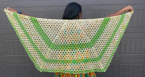An image of a trapezoid shaped crochet shawl made of a lacy x-stitch from a variegated yellow yarn and three stripes of a bright green yarn.