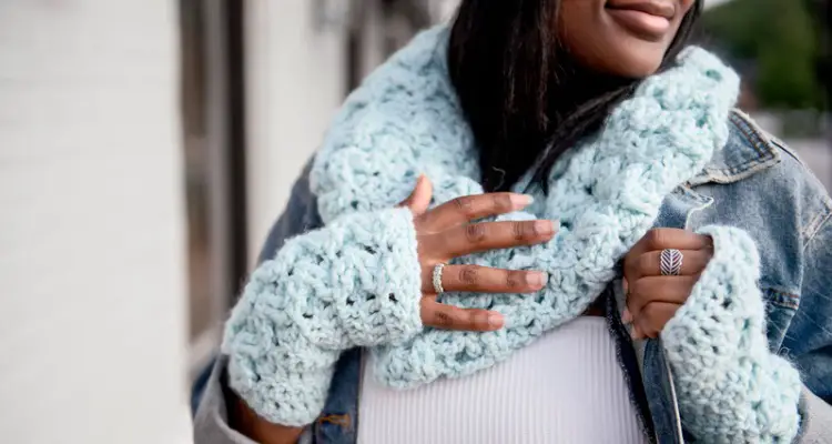 A closeup image of crochet fingerless gloves and cowl made from chunky yarn in a winter blue color.
