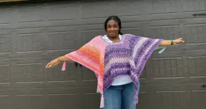 A Black woman is wearing a colorful crochet poncho showing two colors in the granny stitch. You can see 4 of the 6 points and tassels of this hexagon crochet poncho.