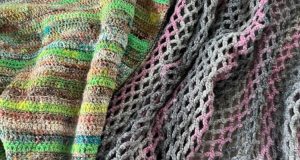 A close up image of the a crochet top made with Noro yarn in shades of green and brown that creates stripes on the left. The right side shows a crochet vest made in a gray and pink sparkle variegated yarn. Both crochet garments are folded to demonstrate drape.