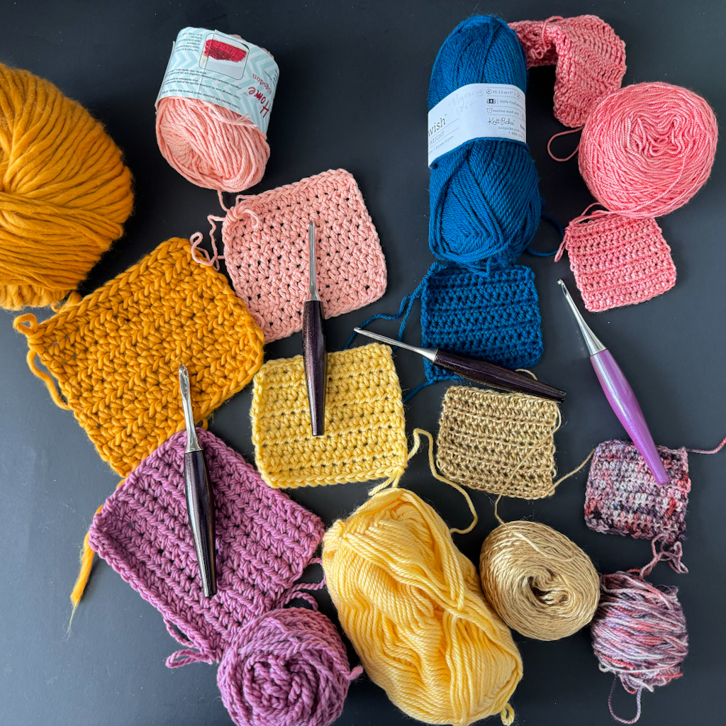 An image of bulky, worsted, DK, sport and fingering weight yarns with four different crochet hooks. Each yarn has a swatch of half double crochet stitches shown. This is to demonstrate the difference in the drape of the fabric.
