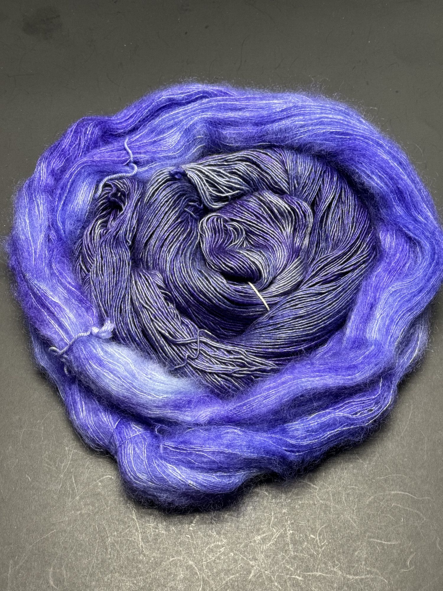 An image of two yarns laying in a circle with the semi-solid purple in the middle surrounded by a fuzzy lace weight yarn.