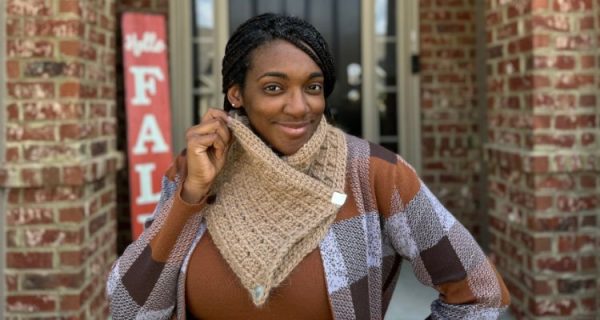 An African American woman wearing a cozy, chunky crochet cowl with two metal buttons standing in front of a door and Hello Fall sign.