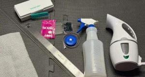 An image of a ruler, blocking combs, spray bottle, steamer, t-pins and a towel on top of a dark gray foam mat.