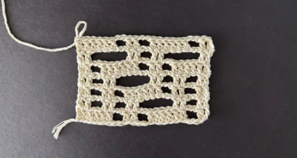 An image of a crochet rectangle made of double crochet and chain spaces in a cream colored yarn for a crochet lace tutorial.