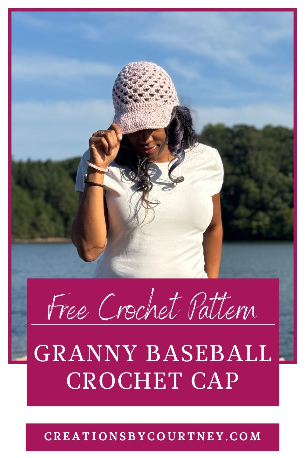 A woman stands outdoors by a lake wearing a light pink crochet baseball cap with a granny stitch design and curved brim, tilting the cap slightly downward. Text on the image reads “Free Crochet Pattern – Granny Baseball Crochet Cap – creationsbycourtney.com.”
