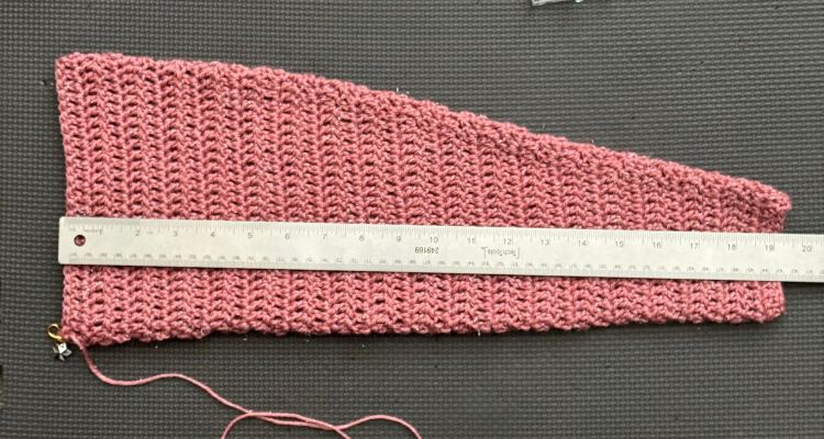 Pink crocheted sleeve piece laid flat with a ruler across the middle showing a width of about 19 inches. The ruler helps demonstrate how to measure crochet sleeve width.